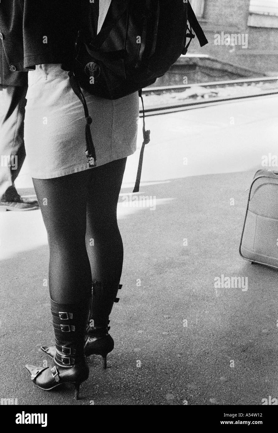 Formschöne Mädchen in einem Mini-Rock und Stiefeln von hinten untere Hälfte stehend auf einem Bahnsteig schwarz / weiß Stockfoto