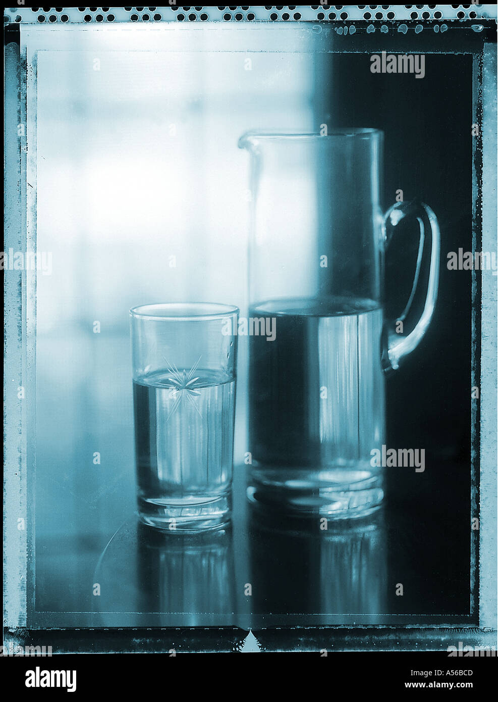 Halb volles Glas Wasser und Krug mit Wasser am Tisch in der Nähe von Fenster Stockfoto