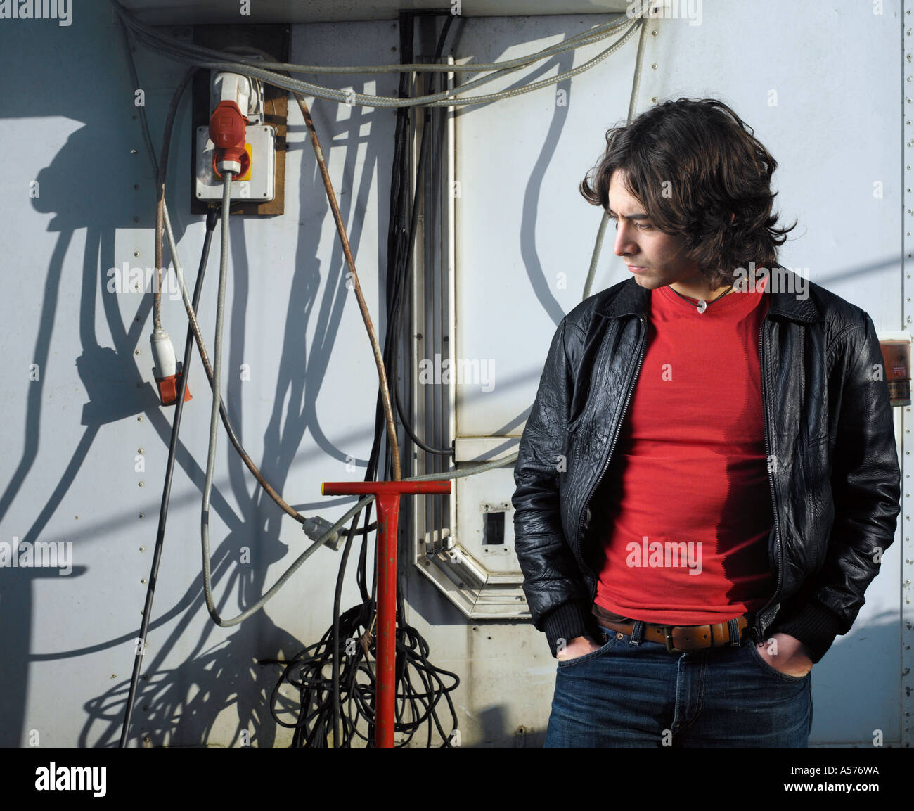 Junger Mann in schwarzem Leder Jacke stehend zwischen Kabeln und Rohrleitungen Stockfoto