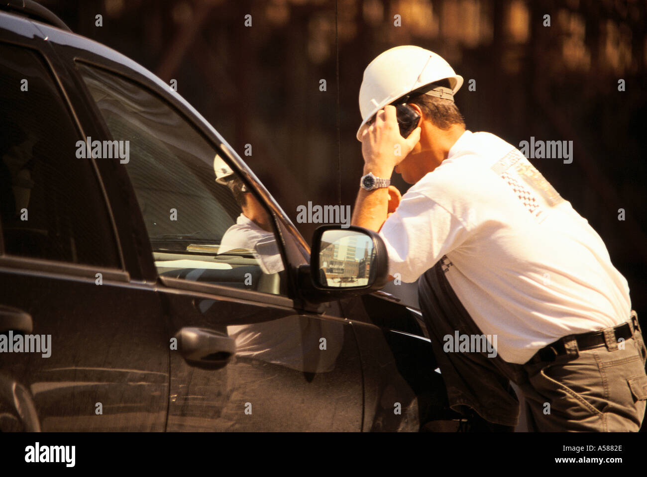 Bühnenmeister in weißen Schutzhelm lehnt sich auf Auto Kotflügel, wie er am Handy spricht Stockfoto