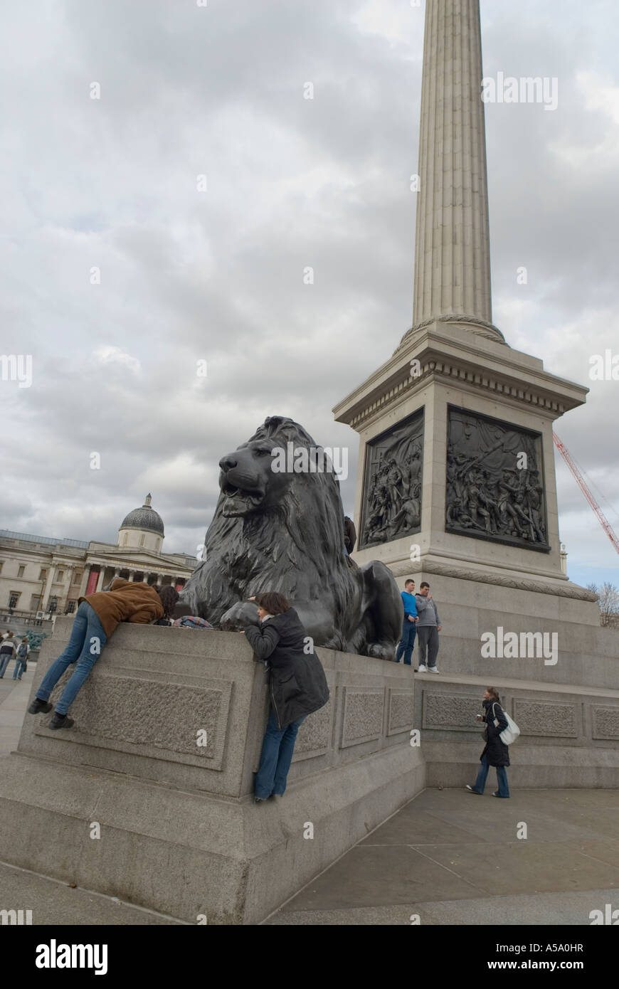 Zwei junge Frauen Klettern auf einen Löwen in Trafalgar square London uk Stockfoto