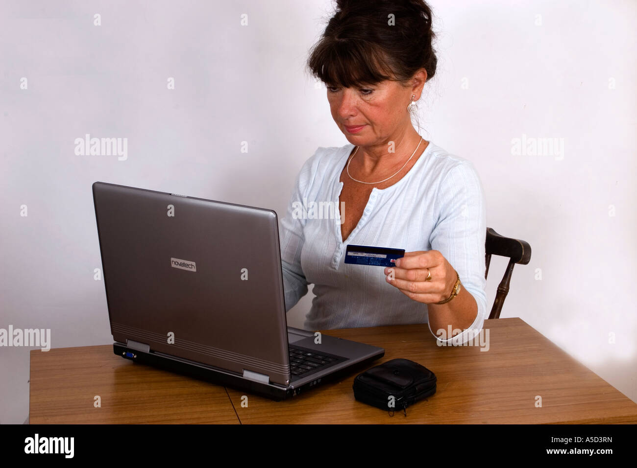 Mittlere gealterte Frau auf Laptop-Computer, die Kredit- oder EC-Karte in der hand halten Stockfoto