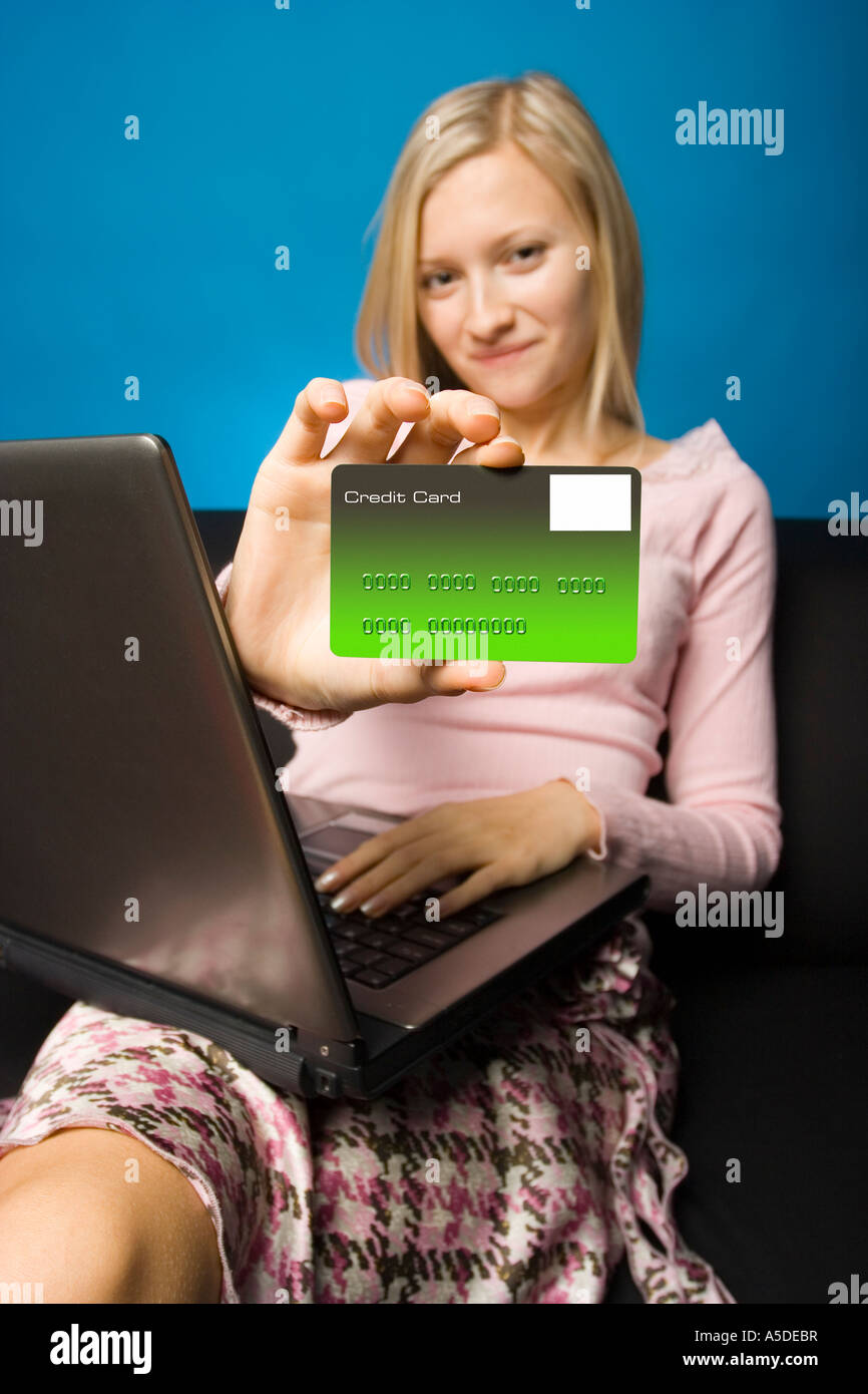 Junge Frau sitzt auf dem schwarzen Sofa mit Laptop und Kreditkarte in der Hand Fokus auf der Karte Gesicht unfocus Stockfoto