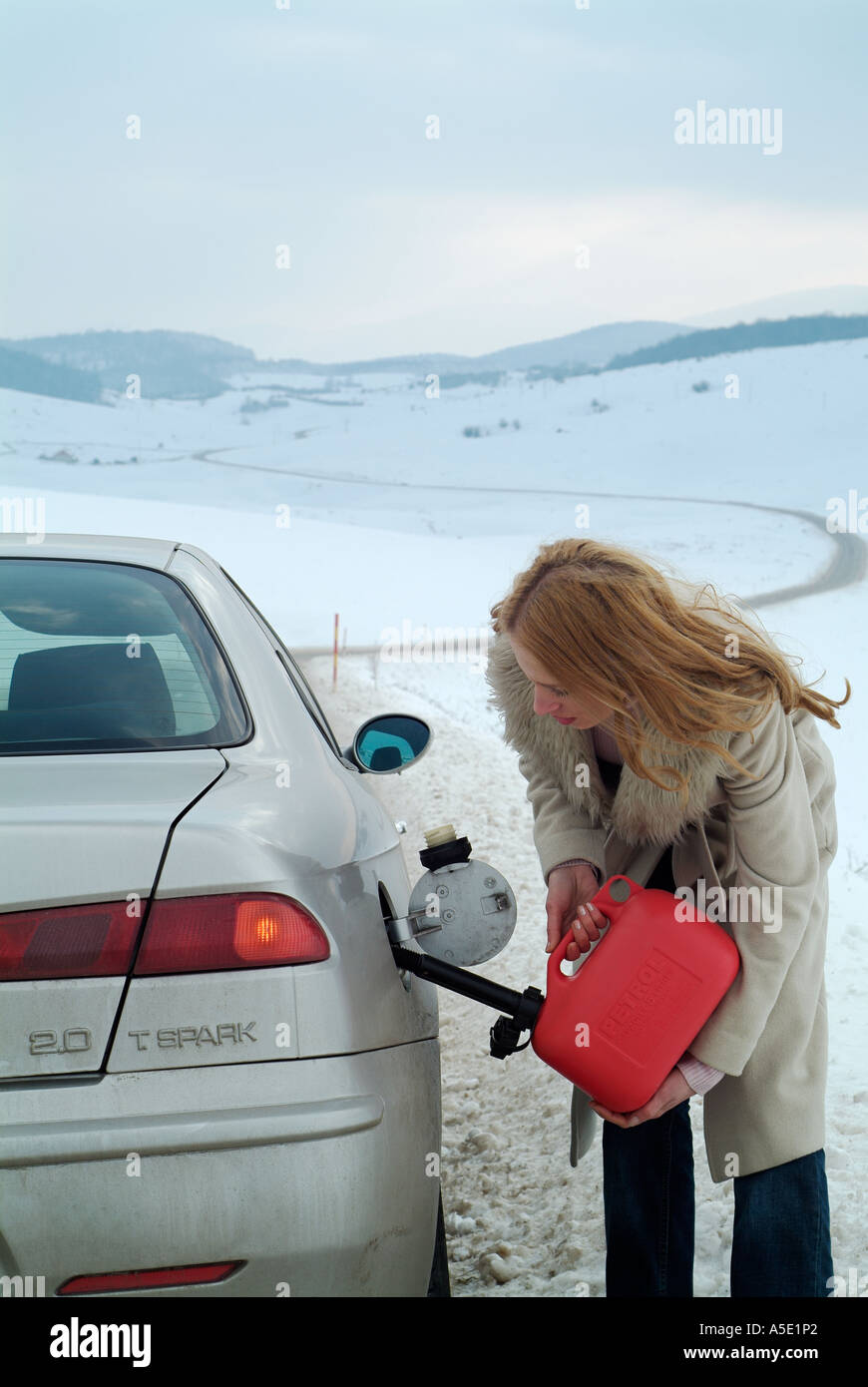 Frau, die ihr Auto mit Benzin nachfüllen, nach dem Bruch nach unten auf einer isolierten ländlichen Straße im Winter Stockfoto