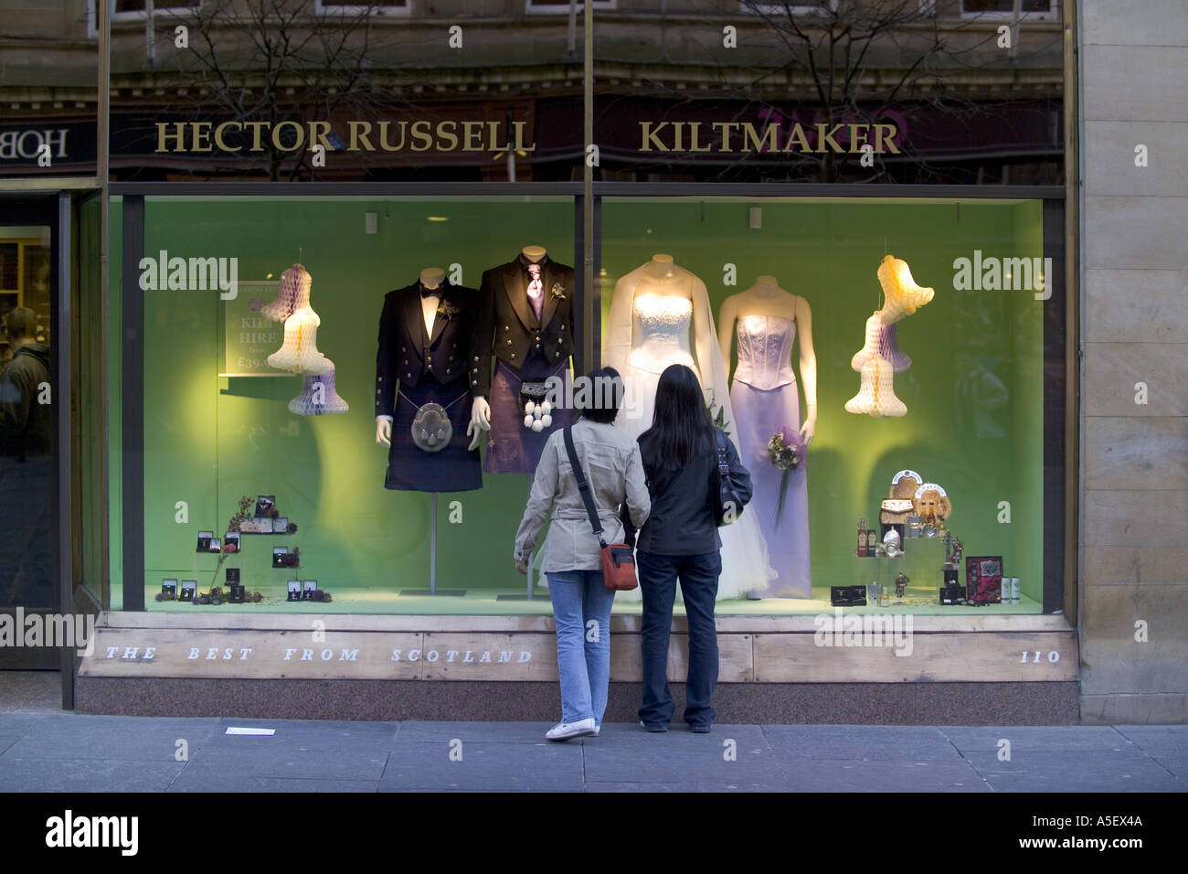 SCHOTTLAND GLASGOW RÜCKANSICHT DER BEIDEN ASIATISCHEN FRAUEN SCHAUFENSTERBUMMEL, BLICK AUF DIE SCHAUFENSTER VON HECTOR RUSSELLS KILT MAKER SHOP Stockfoto