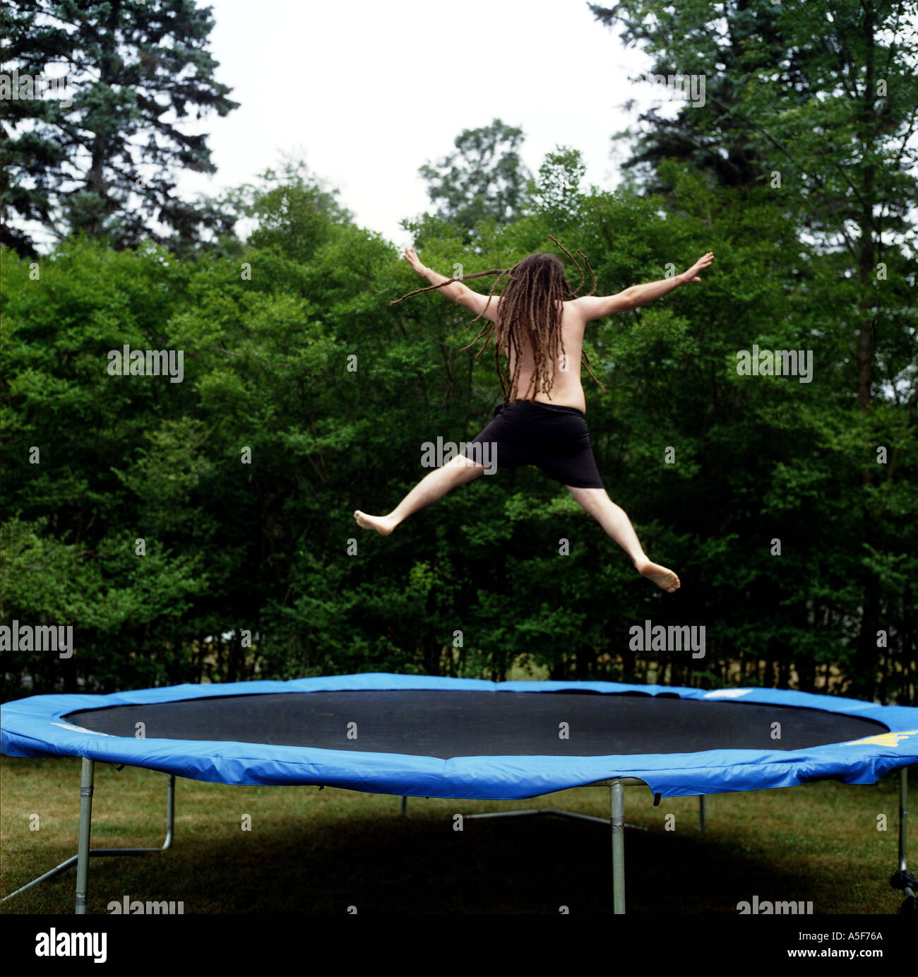 Junger Mann mit Dreadlocks springen auf einem Trampolin außerhalb Stockfoto