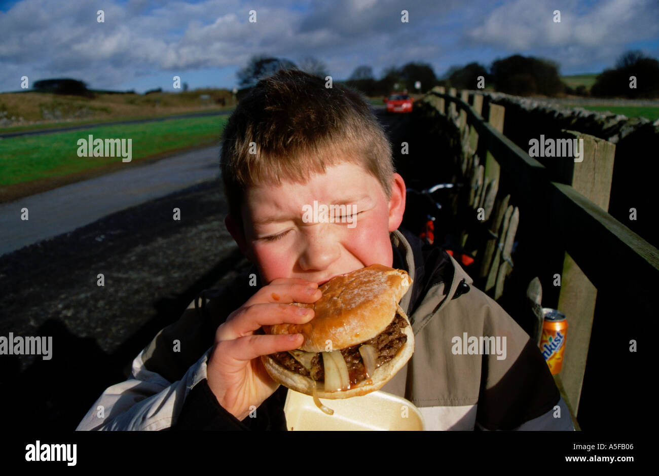 Ein kleiner Junge essen Burger. Beißen in einen großen Burger illustrieren Fettleibigkeit durch Junk-Food Essen. Stockfoto