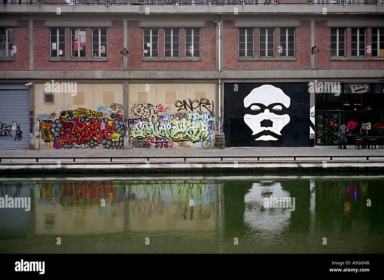 Wandmalereien und Graffiti schmücken die Wand von einem Industriegebäude am Canal Saint-Martin einer Wasserstraße in der Stadt Paris Stockfoto