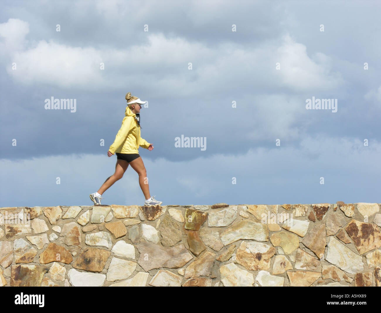 Frau im Wind Jacke und Sport Shorts gehen zügig unter Gewitterhimmel Stockfoto