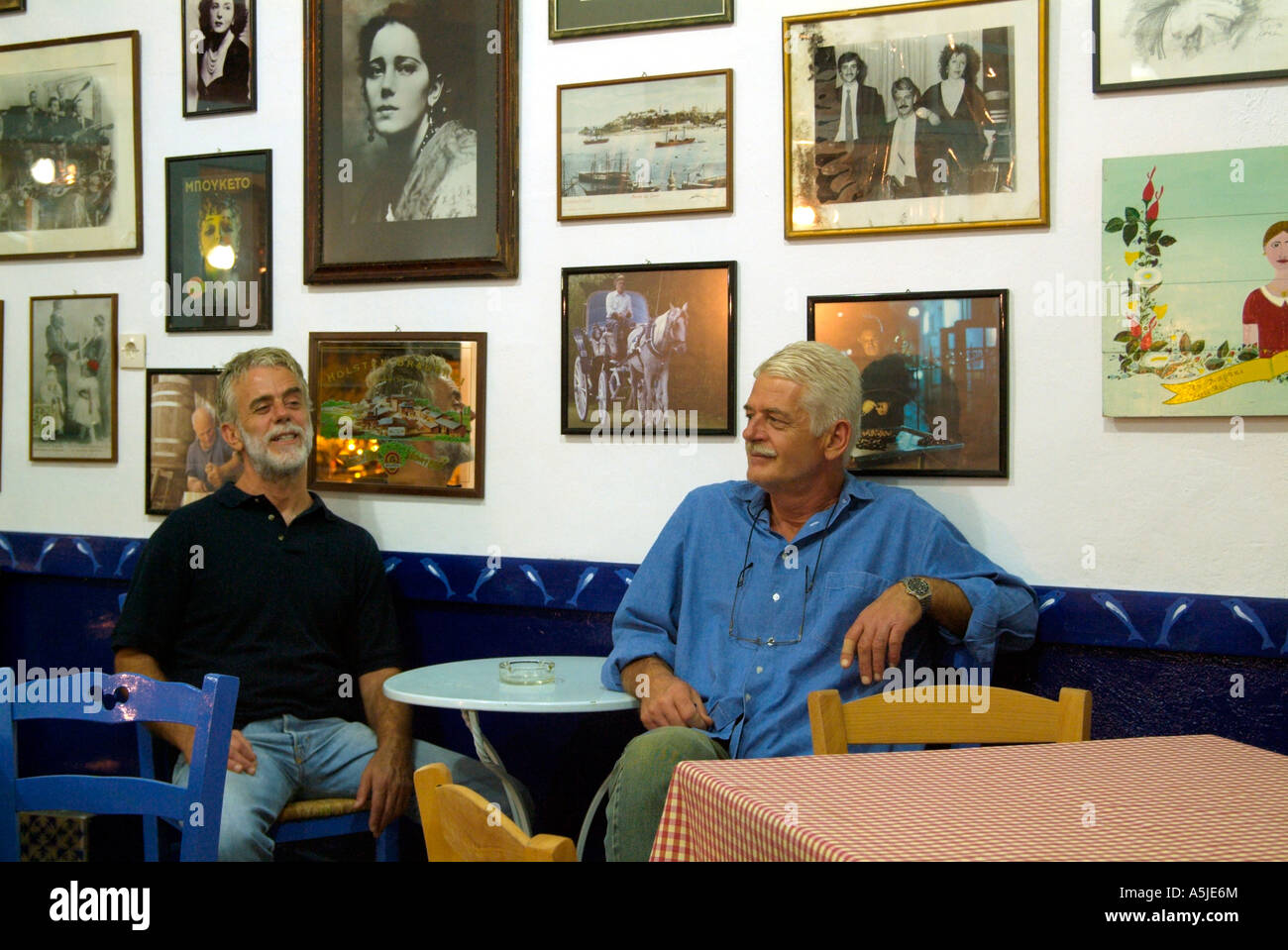 Zwei Brüder mittleren Alters sitzen drinnen in ihrem Restaurant an einer mit Bildern bedeckten Wand. Limenaria, Thassos, Griechenland, Europa Stockfoto