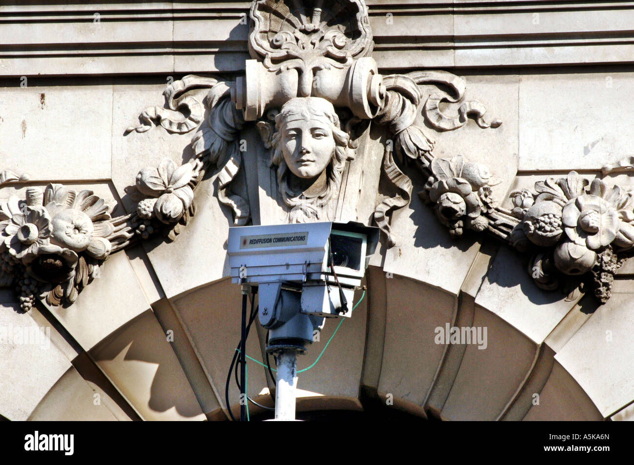 Jugendstil geschnitzten Stein Kopf einer Frau starrt über eine Rediffusion CCTV Überwachungskamera Stockfoto
