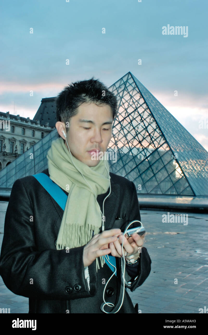 Paris Frankreich, Portrait junger asiatischer Mann, der I POD 'MP3 Player' mit Kopfhörern bei Nacht angehört Pyramide des Louvre-Museums Jungen überwintern Stockfoto