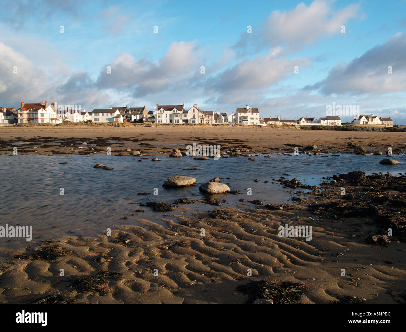 Sandstrand bei Ebbe Rückblick auf Strandpromenade Häuser im Dorf mit Sand Wellen im Vordergrund im Winter Rhosneigr Anglesey Stockfoto