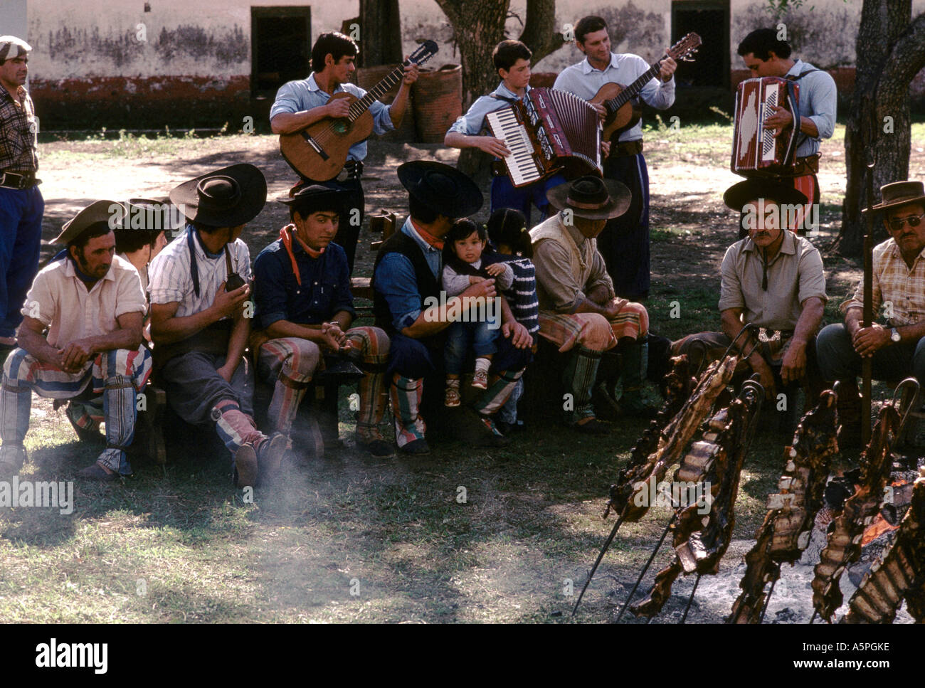 Gauchos, die Standortwahl herum wartet ein Scampispieß Mittagessen mit Lamm und Rind auf einem open Air Feuer, wie sie Volksmusik, Argen hören Stockfoto