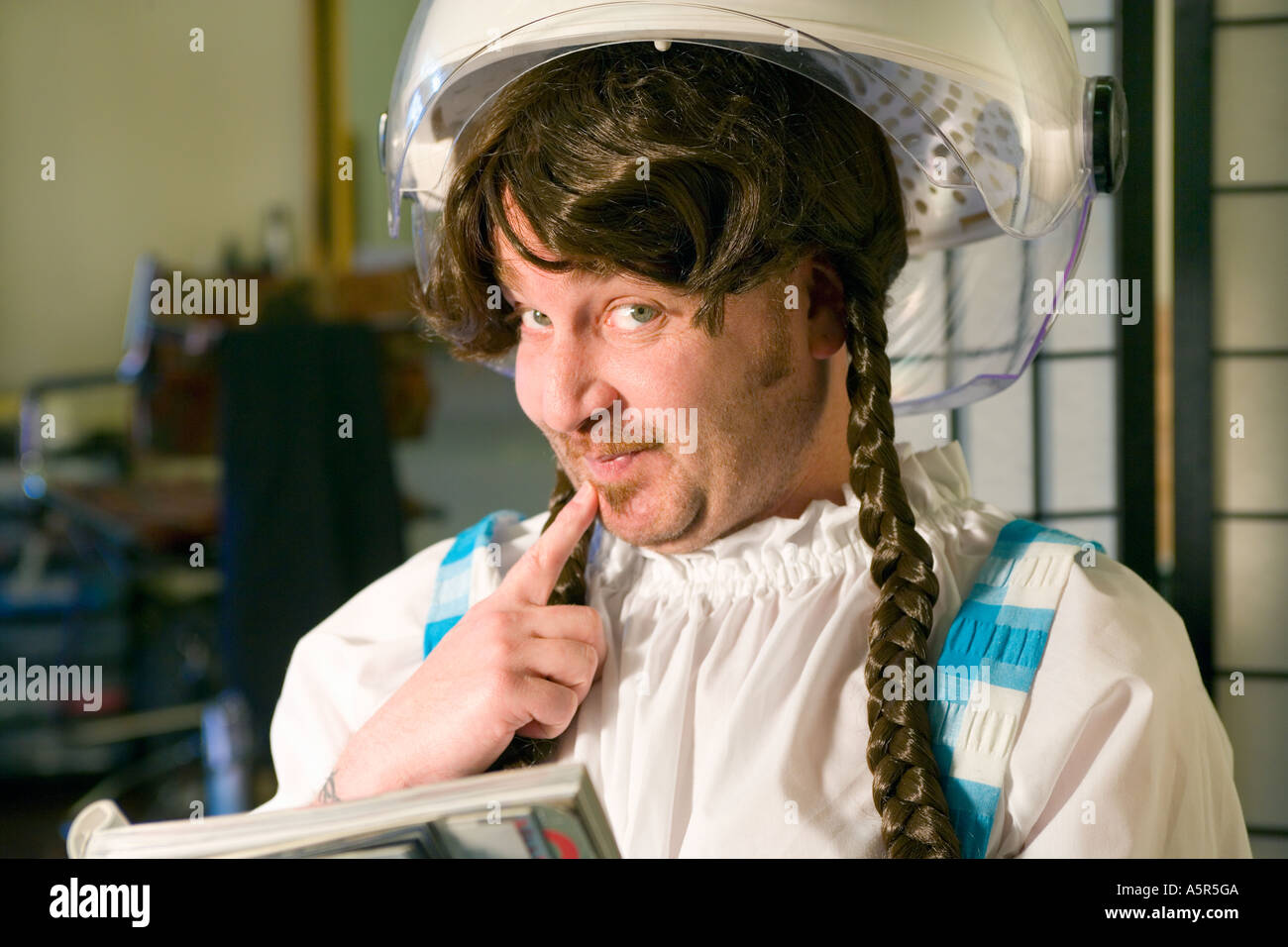 Mann, gekleidet wie eine Frau sitzt in einem Friseursalon unter Haartrockner Stockfoto
