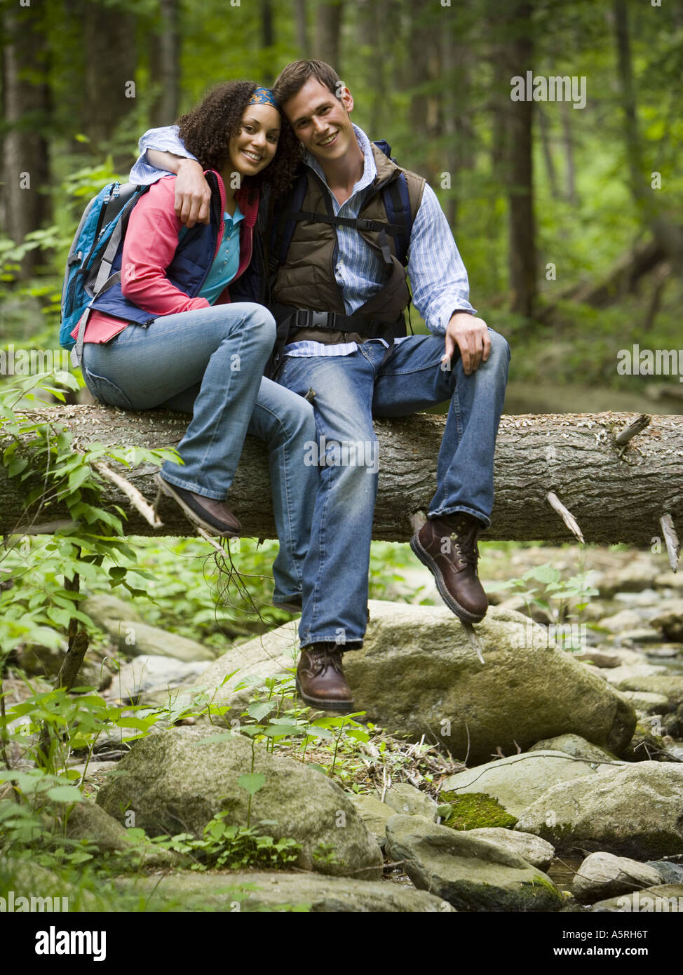 Porträt eines jungen Paares auf einen umgestürzten Baum sitzend Stockfoto