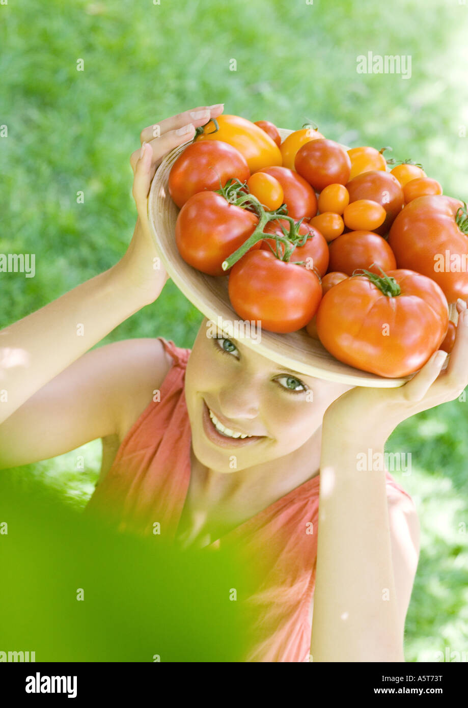 Frau Holding Schüssel voller Tomaten oben auf Kopf Stockfoto