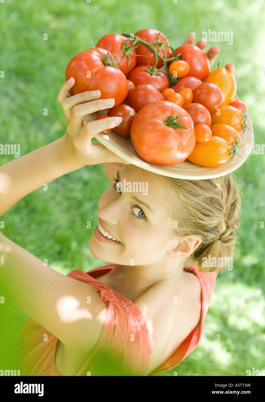 Frau Holding Schüssel voller Tomaten oben auf Kopf Stockfoto