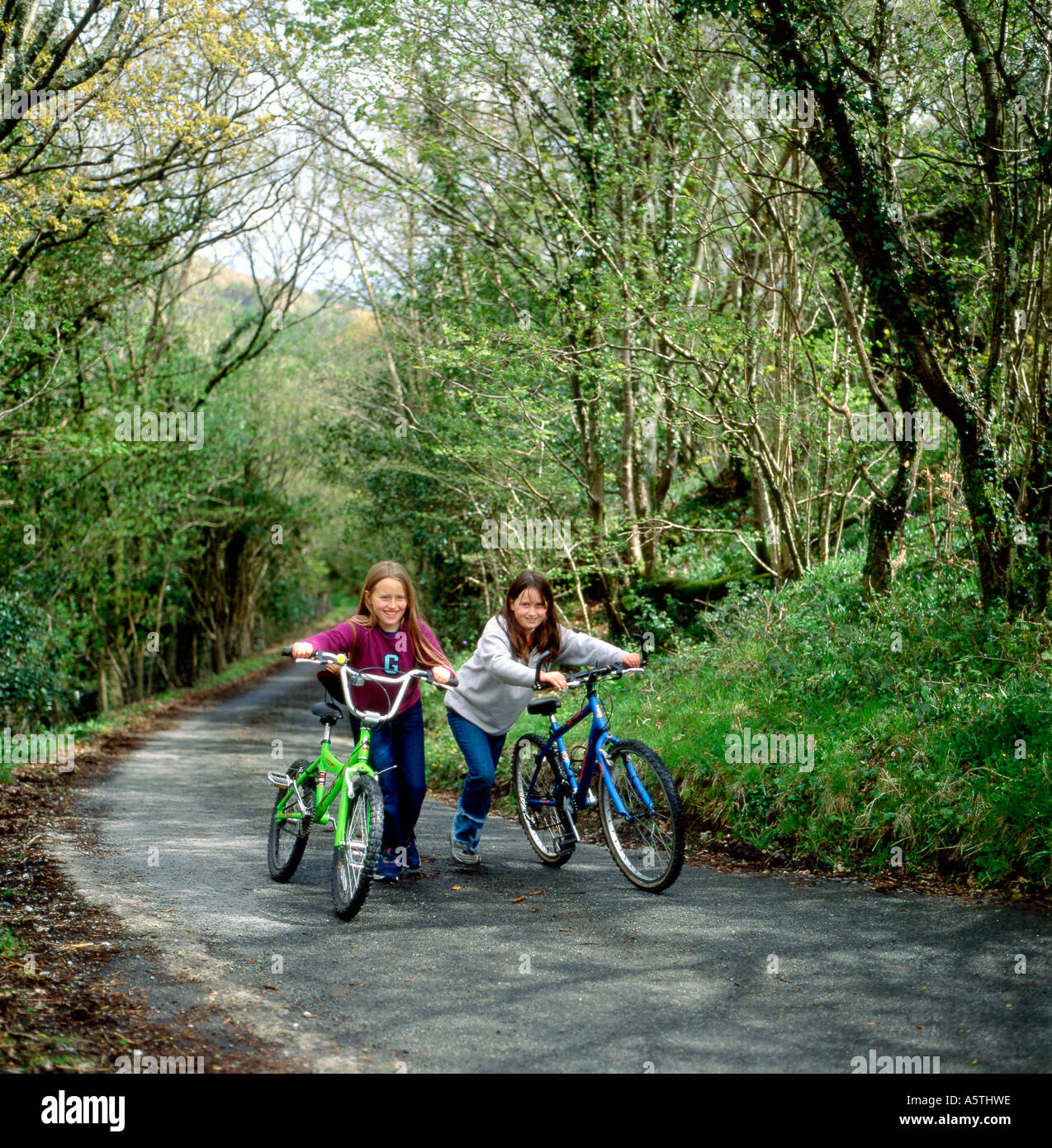 Fröhliche Jugendliche Mädchen junge Radfahrer Kinder im Frühling in Carmarthenshire Wales UK KATHY DEWITT Fahrräder auf einem Hügel auf einer Landstraße schieben Stockfoto