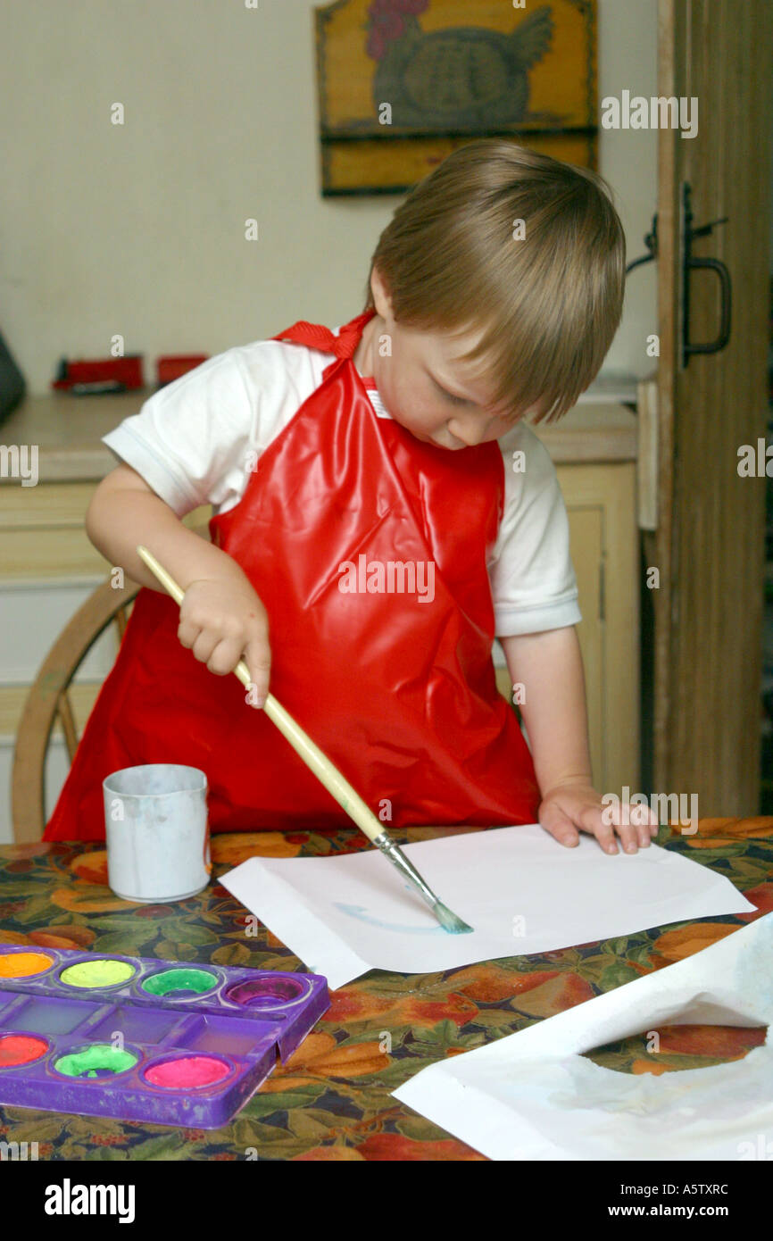 drei Jahre alter Junge ein Bild am Küchentisch trägt eine rote Schürze Stockfoto