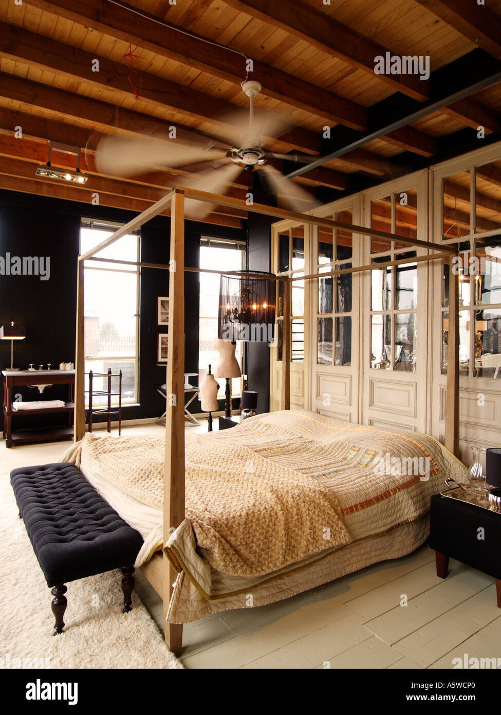Stilvolle Schlafbereich im Loft-Apartment mit großen Ventilator über dem Bett und alten Türverkleidungen mit spiegeln in Ihnen Stockfoto