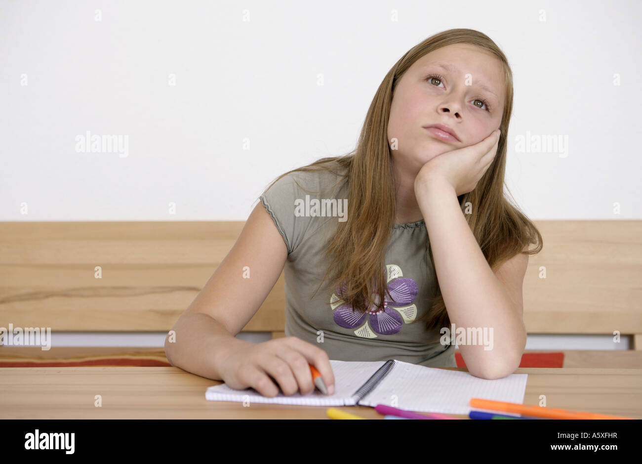 Mädchen mit Stift und Übungsbuch auf Schreibtisch wegschauen Stockfoto