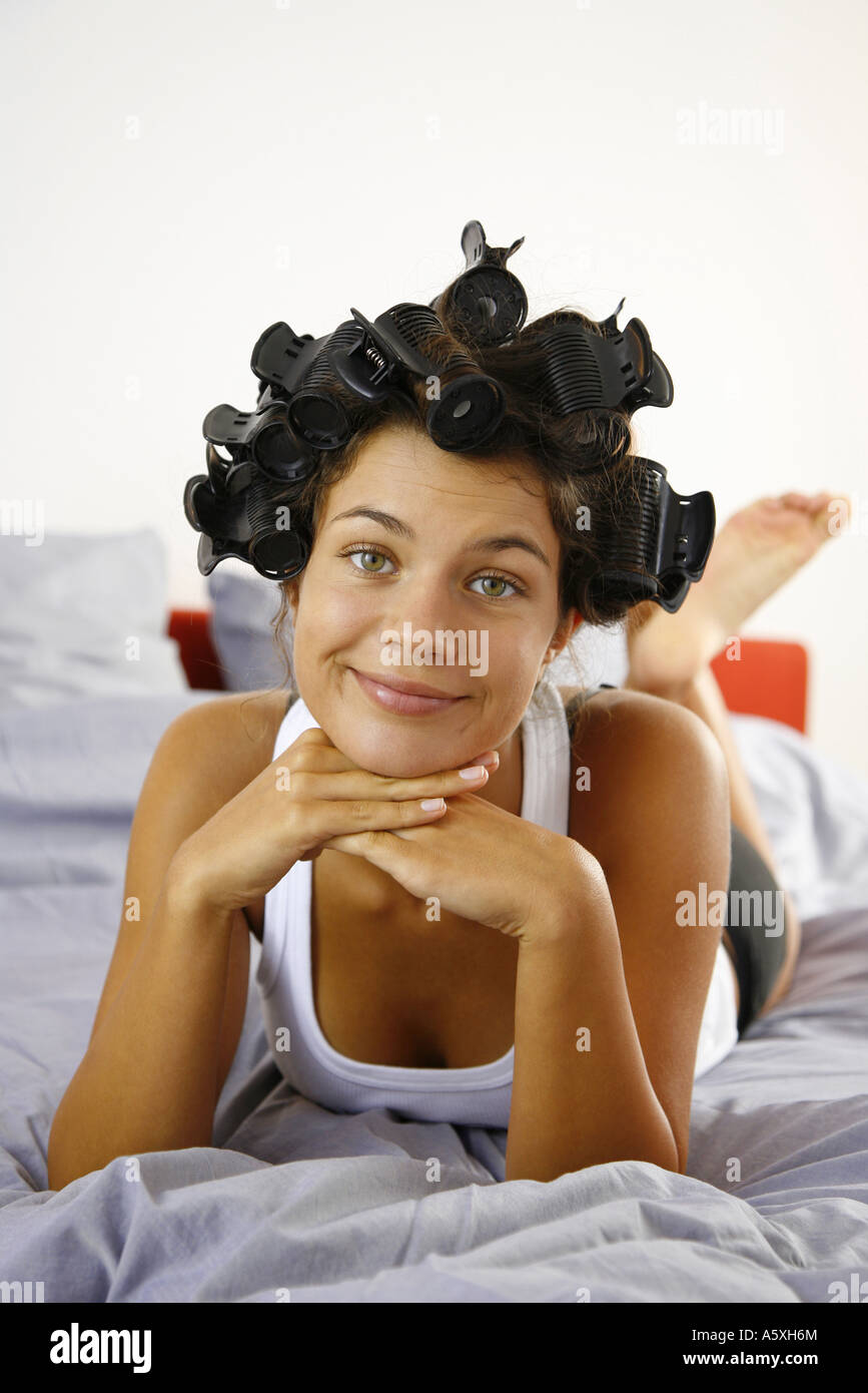 Junge Frau trägt Rollen in Haaren auf Bett lächelnd Porträt Stockfoto