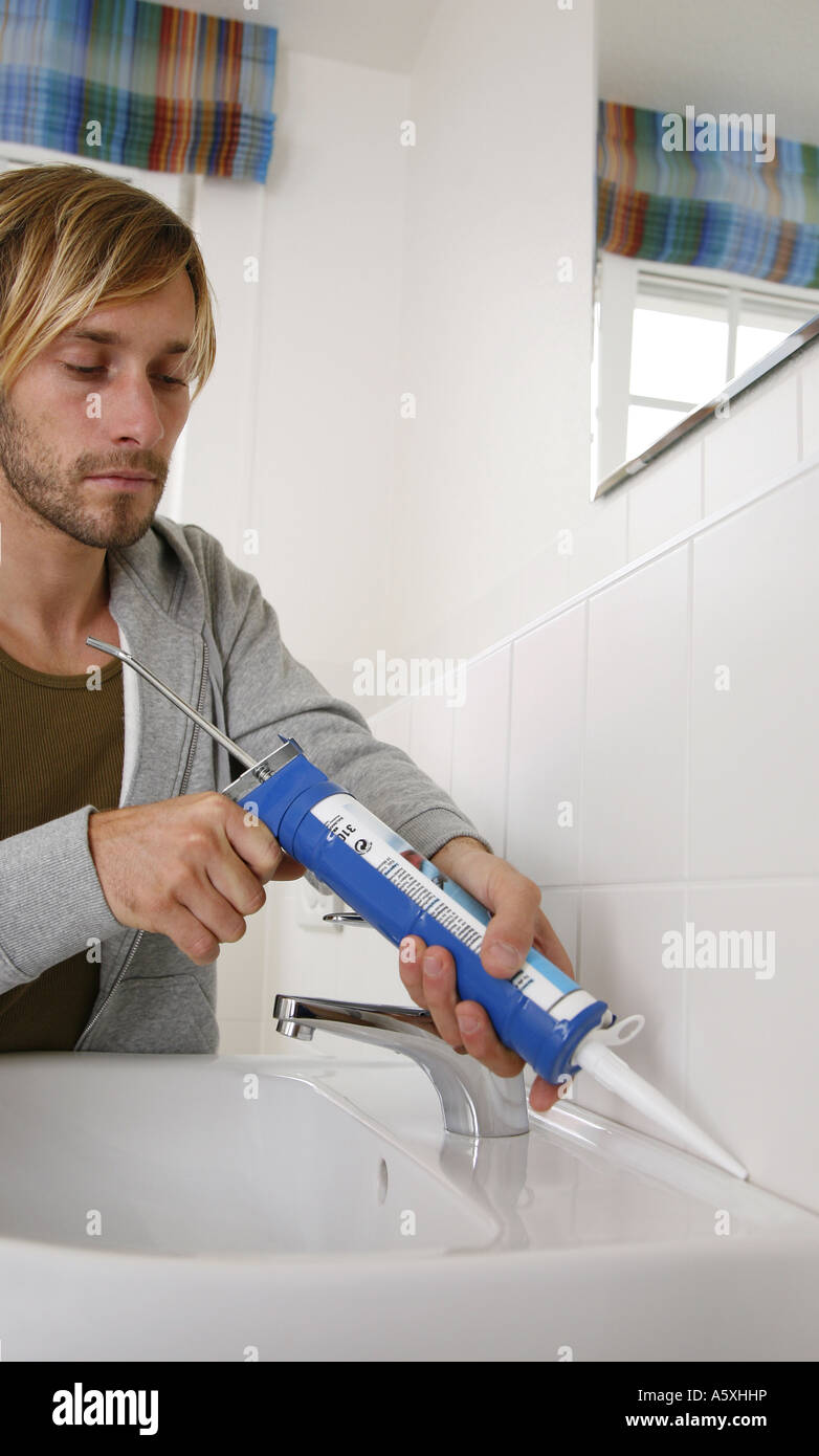 Junger Mann mit einer Silizium-Dosierpistole auf ein Waschbecken im Badezimmer Stockfoto