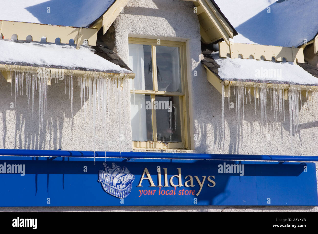 Geneigtes schneebedecktes Dach mit harten spitzen Eiszapfen auf Alldays Shop in Braemar Scotland UK. Februar Sonnenschein mit Eiszapfen hängen von den Dächern Stockfoto