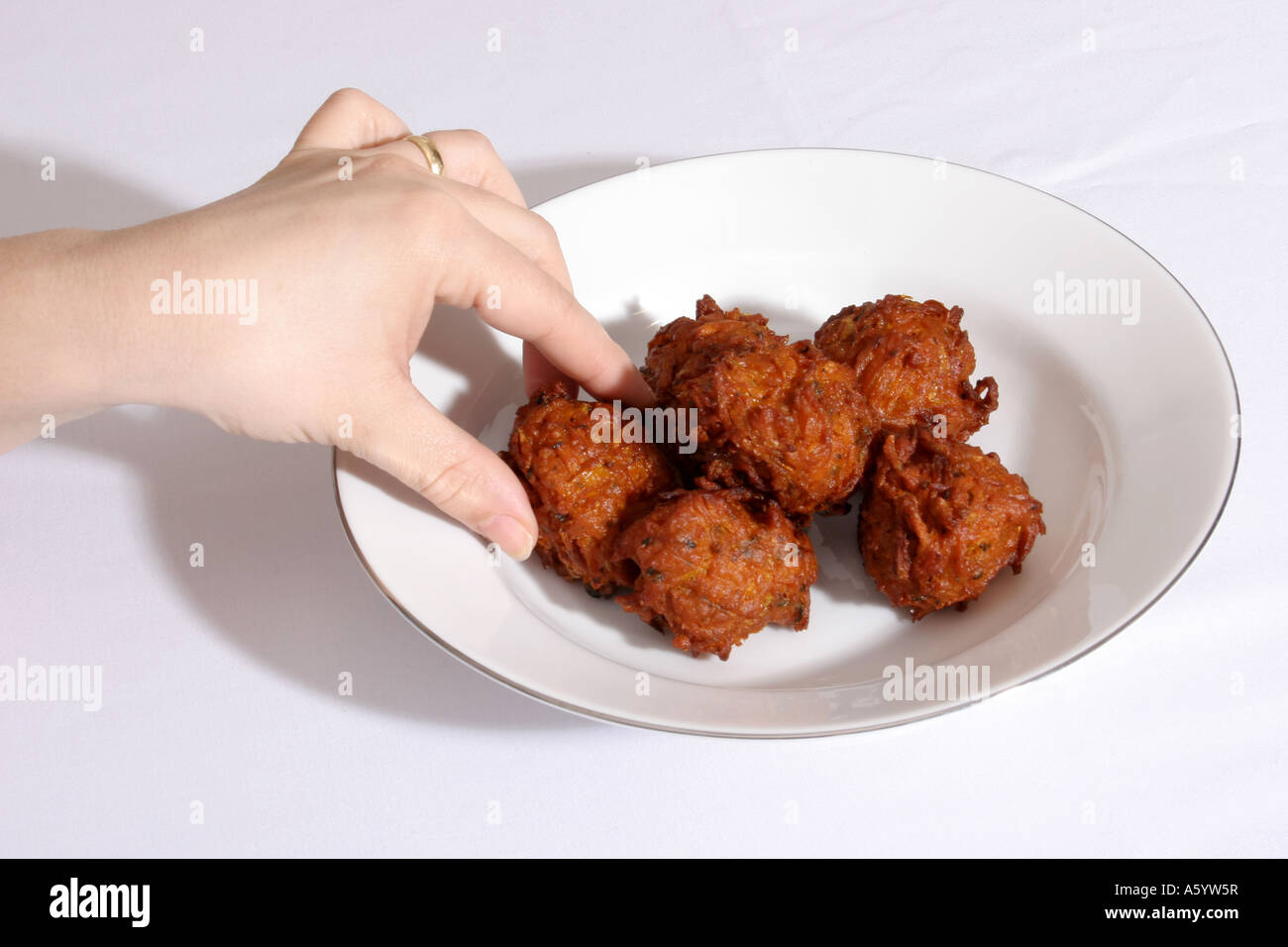 Eine Hand, eine große Zwiebel-Bhajis aus einer Platte nehmen. Stockfoto