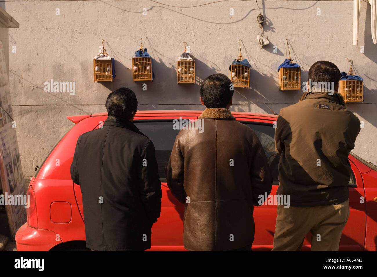Männer stehen Vogelkäfige hinter einem roten Auto in der Altstadt, Shanghai, die Volksrepublik China zu betrachten, Stockfoto