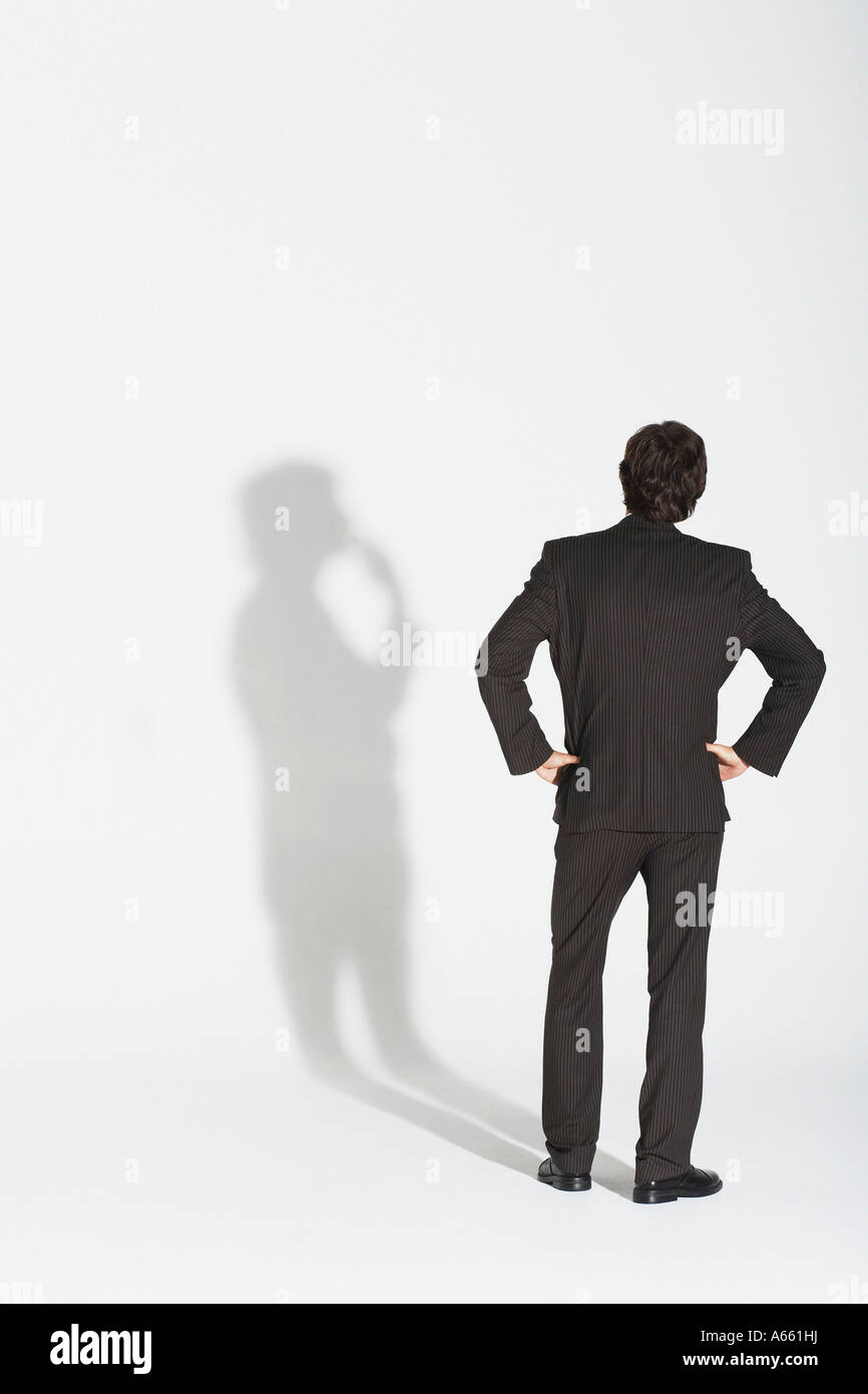 Junger Geschäftsmann stehend, die Hände auf Hüfte, Streit mit eigenen Schatten zurück Ansicht Stockfoto