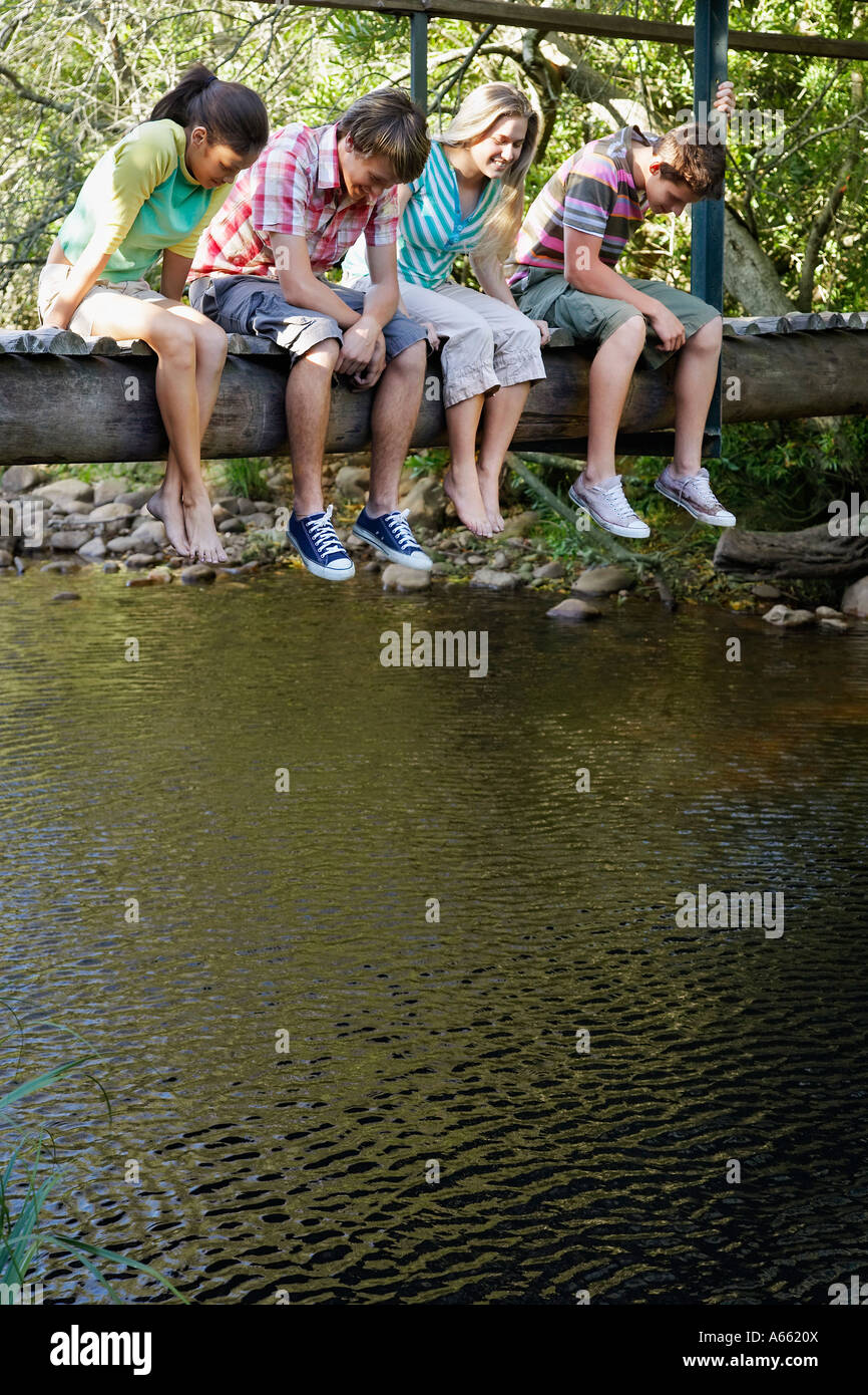 Vier Jugendliche (16-17 Jahre) sitzt auf der Holzbrücke, blickte auf Stream, Lächeln Stockfoto