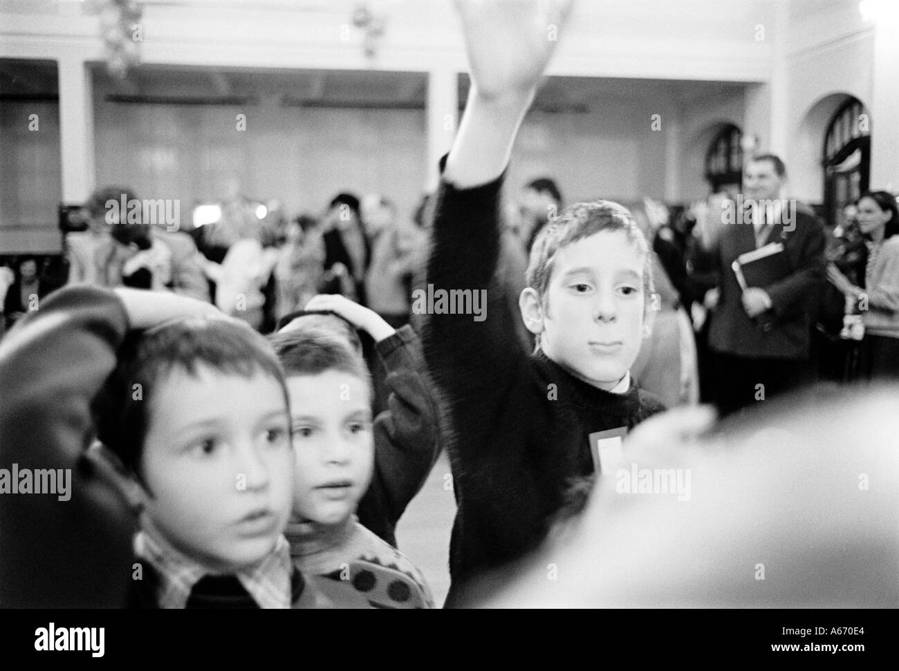 Ein Prager jüdischer Junge hebt seine Hand um eine Channukah Quizfrage zu beantworten, während zwei kleinere jungen geblendet stehen Stockfoto