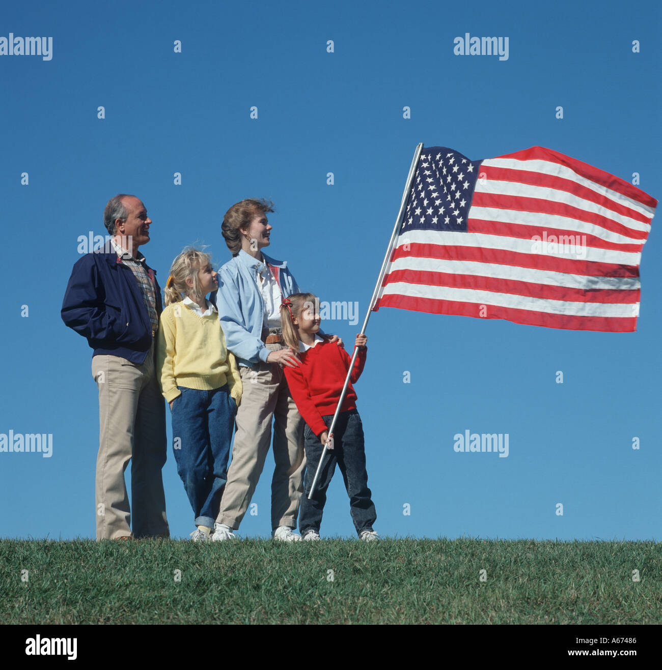 Vierköpfige Familie mit USA-Flagge auf Hügel, die im Wind wehen Stockfoto