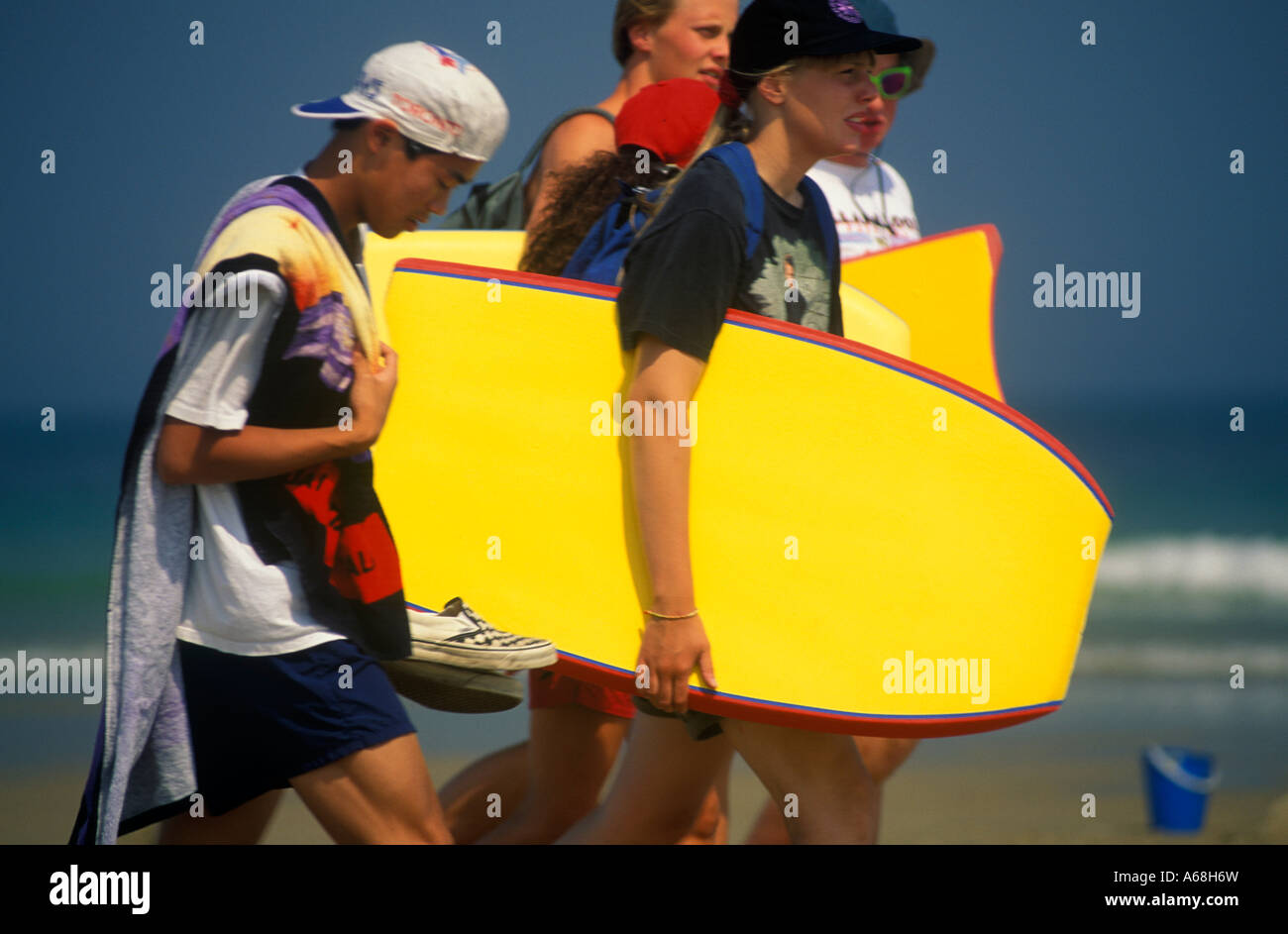 Gruppe von Jugendlichen zu Fuß entlang des Strandes mit Boogie-boards Stockfoto