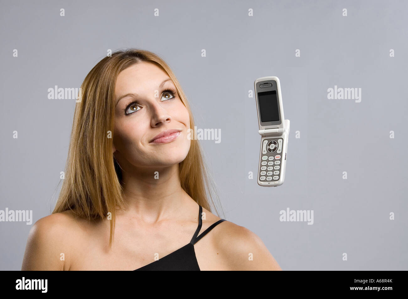Schöne blonde Frau in schwarze schulterfreie Top Interaktion mit einem schwebenden Motorola Razr Handy. Stockfoto