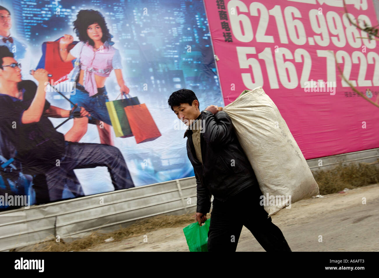 Wanderarbeitnehmer mit seinem Gepäck geht vorbei an einer Plakatwand mit China' s modernen Lebens für eine Gewerbeimmobilie in Peking 2006 Stockfoto