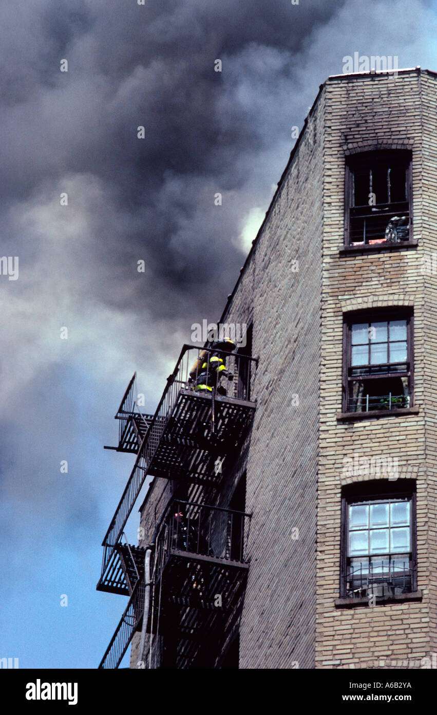 Feuerwehrmänner betreten ein brennendes Wohngebäude über eine Feuertreppe. Feuerwehrleute klettern Treppen, um das rauchgefüllte Mietshaus zu betreten. Die Bronx New York Stockfoto