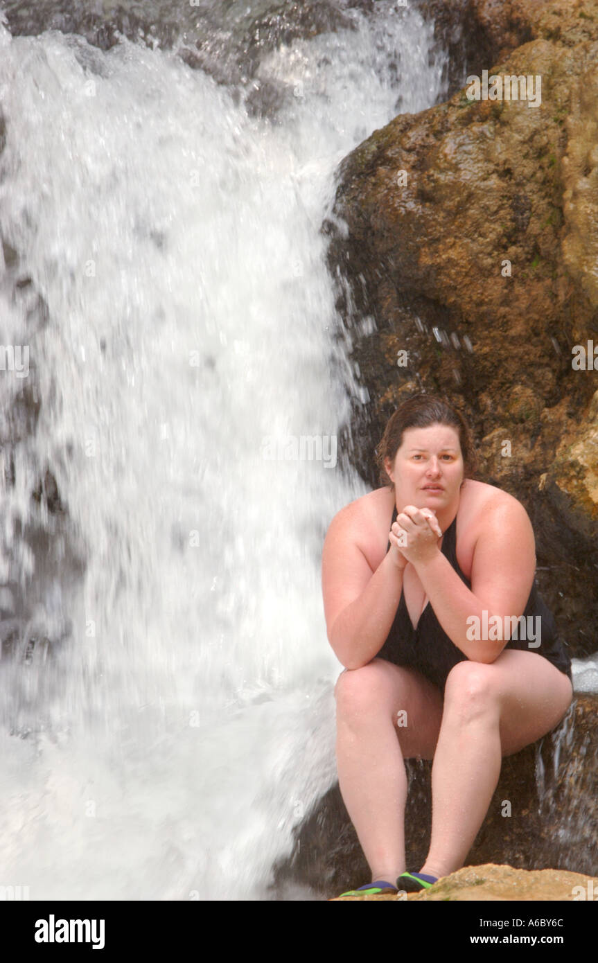 Vertikale Farbbild einer jungen Frau im Badeanzug sitzt auf einem Felsen vor einem Wasserfall Stockfoto