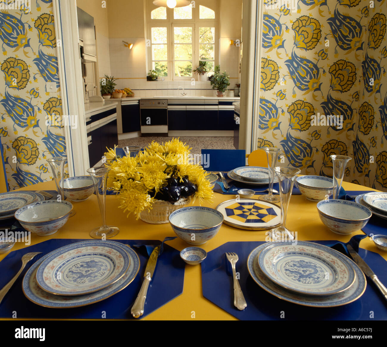 Blaue Servietten und Geschirr auf gelbe Tischdecke im Esszimmer mit gelb  und blau gemusterten Tapeten und offene Tür zur Küche Stockfotografie -  Alamy