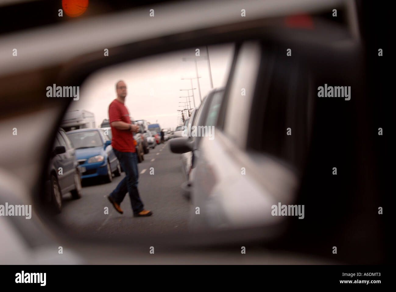 EIN MANN IM BILD IN EINEM FLÜGEL SPIEGEL ÜBERQUERT DIE AUTOBAHN ZU FUß IM STAU Stockfoto