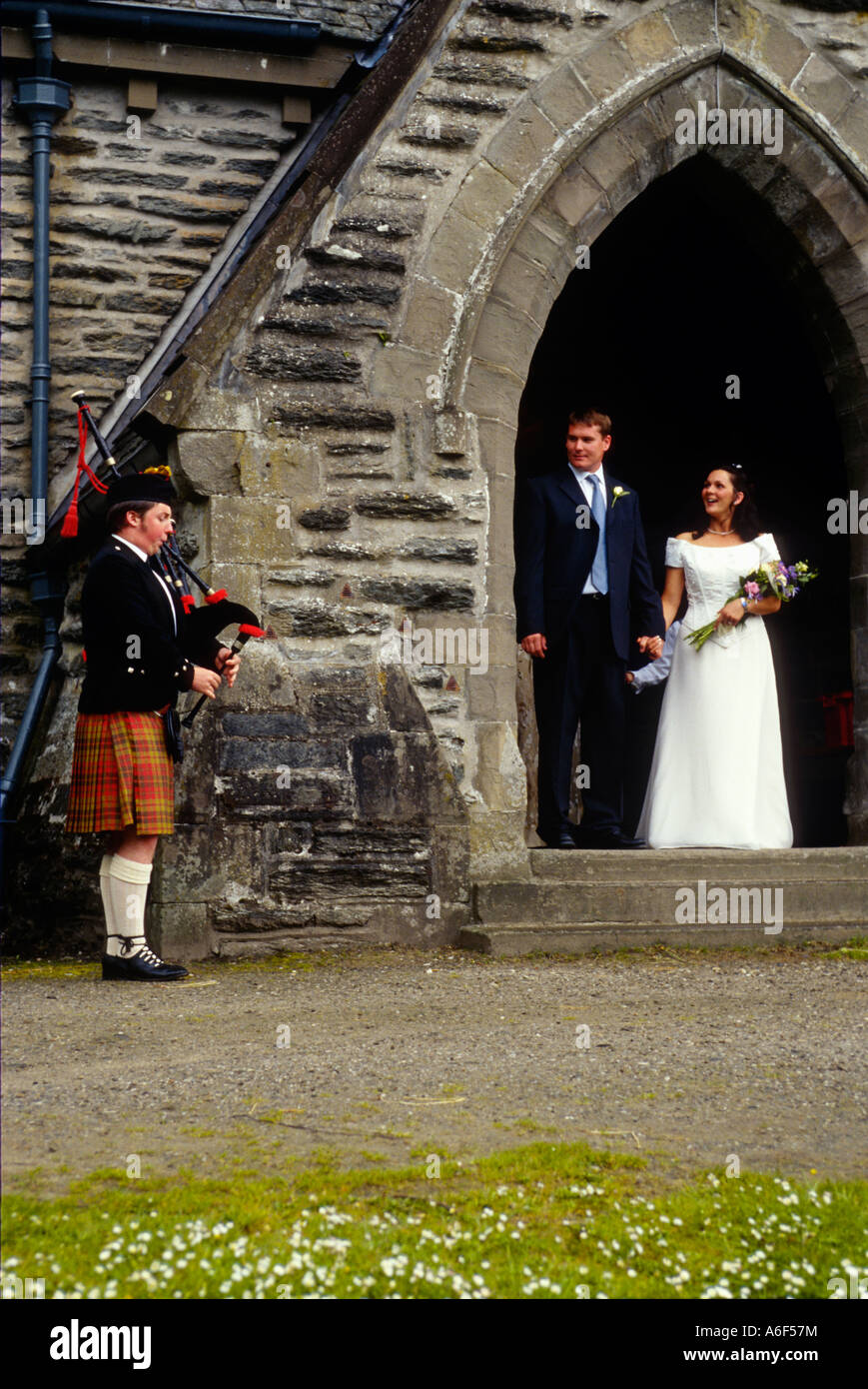 Schottland Balquhidder männlichen Dudelsackpfeifer spielen außerhalb des 19. Jahrhunderts Pfarrei Kirche Braut und Bräutigam stehen in Bogen Hochzeitszeremonie Stockfoto