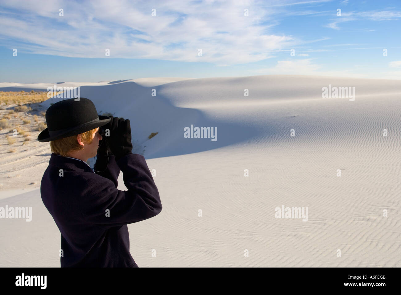 Mann mit Mantel und Bowler Hut Blick durch ein Fernglas auf weiße Sanddüne Wüste Stockfoto