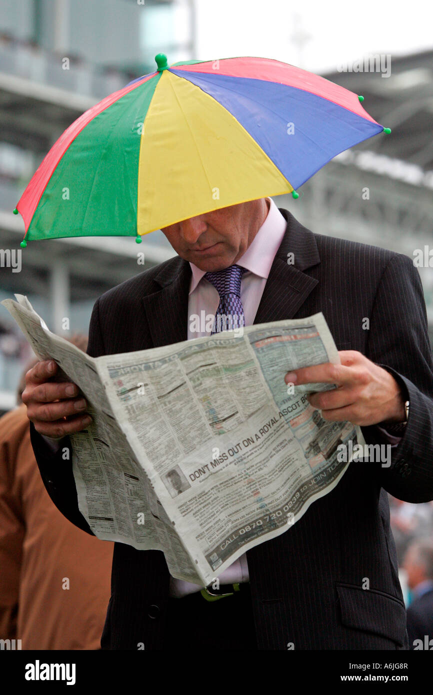 Mann trägt einen Regenschirm-Hut, lesen eine Zeitung am Royal Ascot Pferderennen, York, Großbritannien Stockfoto