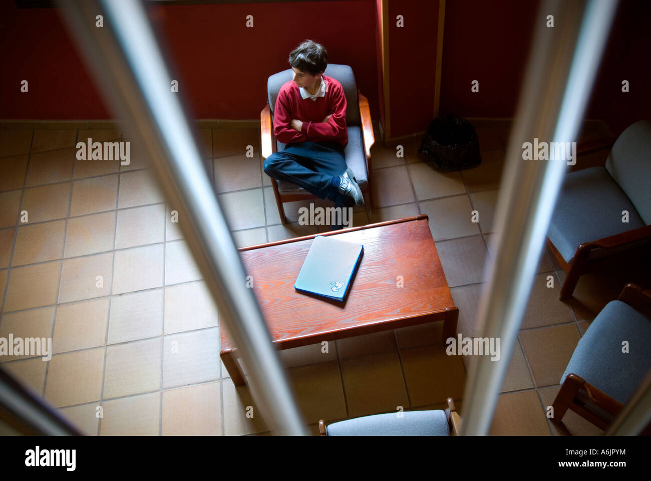 Ängstlich Junior Schuljunge mit Arbeit Ordner warten allein in sichere Schule-Tagungsraum Stockfoto