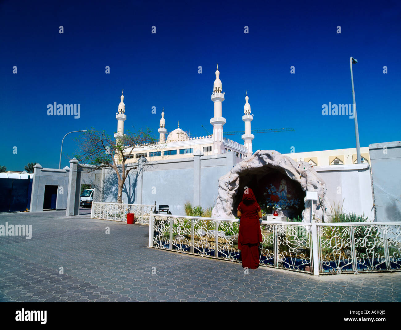 Dubai Vereinigte Arabische Emirate Christian Woman beten am Schrein des St. Mary außerhalb von Str. Marys katholische Kirche mit Minaretten im Hintergrund Stockfoto
