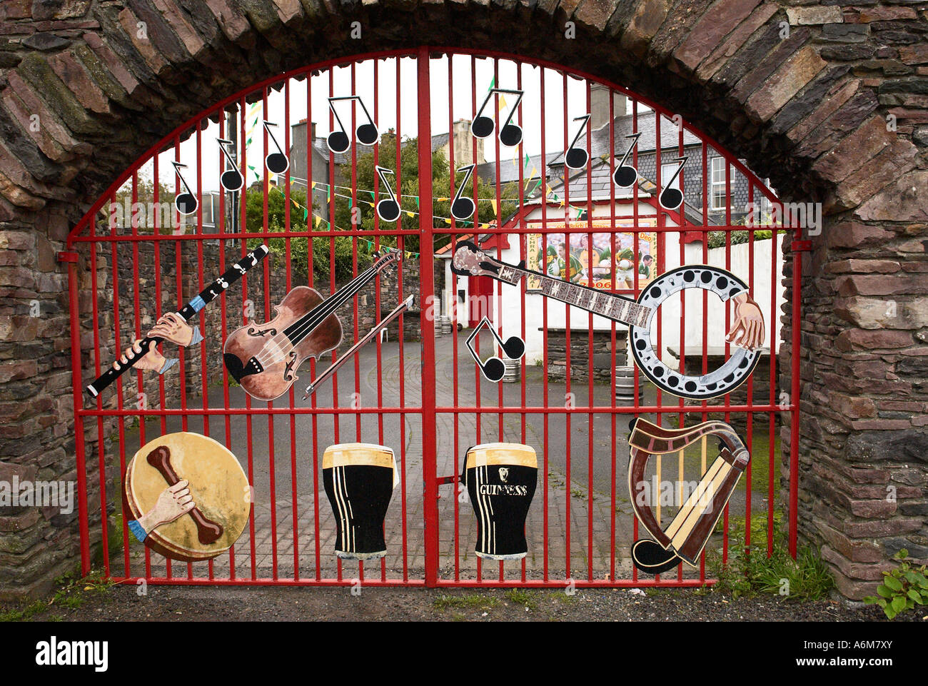 Roten Eisentor mit Guinness Bier Symbole führt durch einen gemauerten Bogen in eine Kneipe in Dingle Stadt County Kerry Irland-Musik Stockfoto