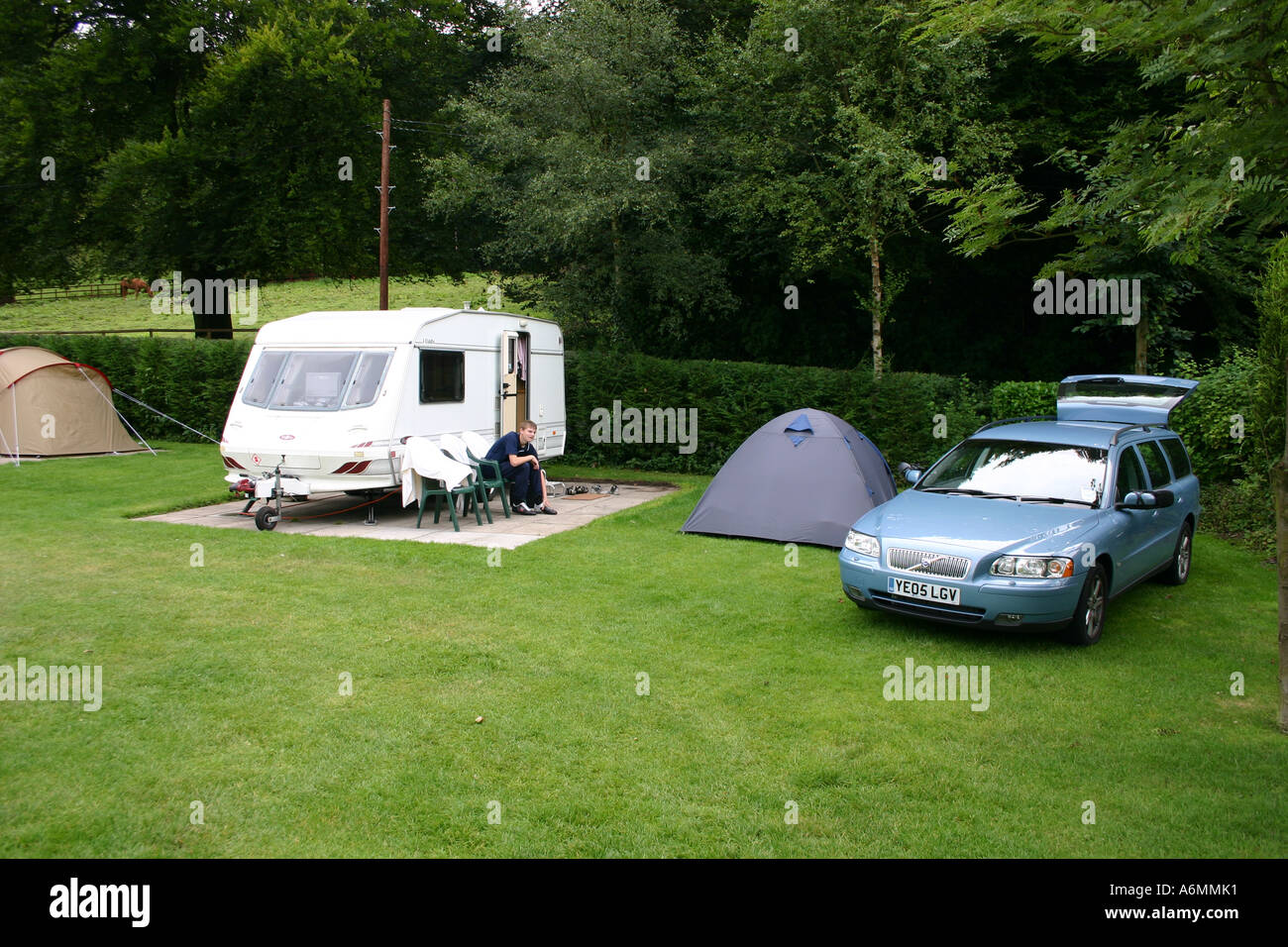 Teenager, draußen Wohnwagen mit Zelt und Volvo V70 estate Stockfoto