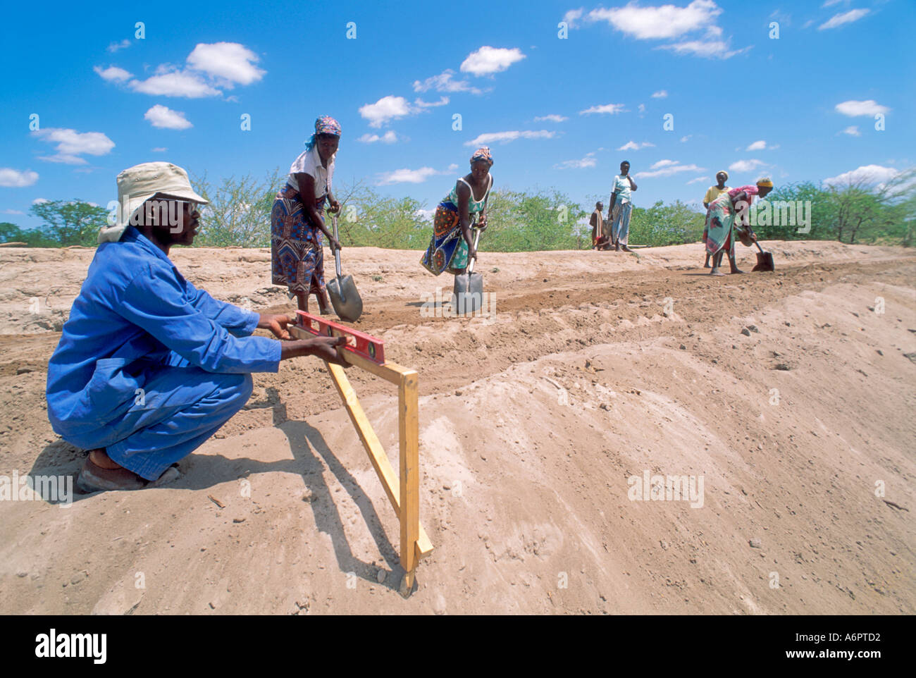 Surveyor Überprüfung der Ebenen und Frauen arbeiten an einem kommunalen Staudammbau-Projekt, um ein Reservoir für die Wassererhaltung während der Dürre zu schaffen. Simbabwe Stockfoto